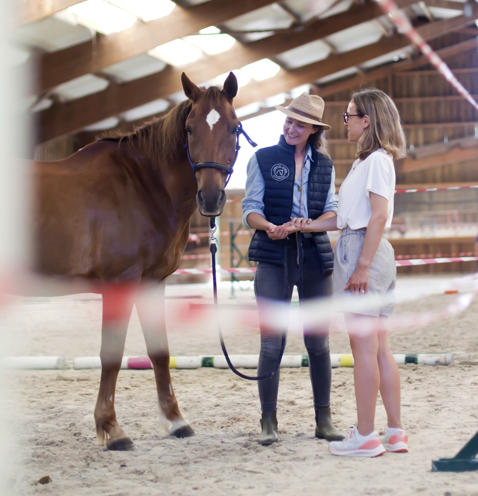 Deux participantes échangent aux côtés d'un cheval dans un manège